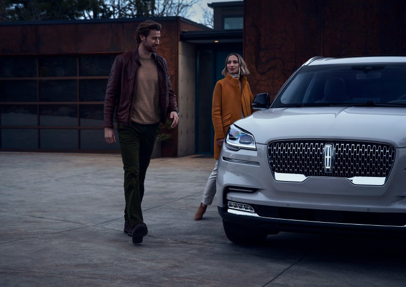 A man and a woman approaching a 2024 Lincoln Aviator® SUV, which illuminates certain lights when they are close | Bozard Lincoln in Saint Augustine FL