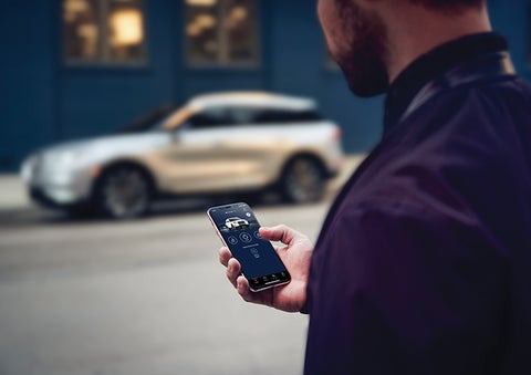 A person is shown interacting with a smartphone to connect to a Lincoln vehicle across the street. | Bozard Lincoln in Saint Augustine FL