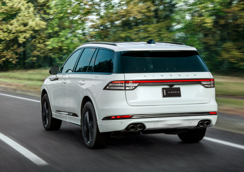 A white 2025 Lincoln Aviator® SUV is being driven away down a road lined with colorful trees. | Bozard Lincoln in Saint Augustine FL
