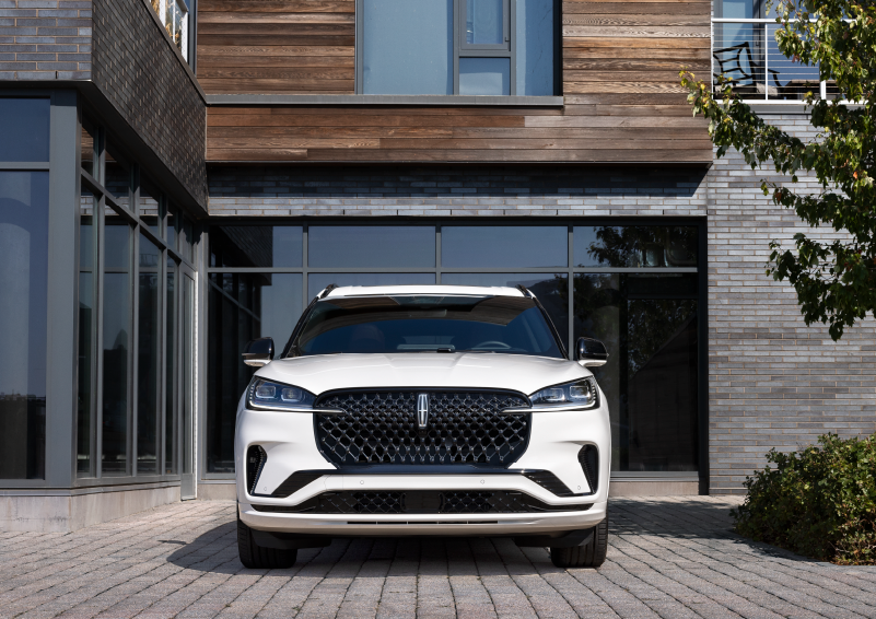 A white 2025 Lincoln Aviator® SUV is shown parked outside a modern building with gray brick and wood accents. | Bozard Lincoln in Saint Augustine FL