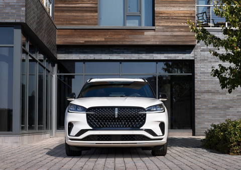 A white 2025 Lincoln Aviator® SUV is shown parked outside a modern building with gray brick and wood accents. | Bozard Lincoln in Saint Augustine FL