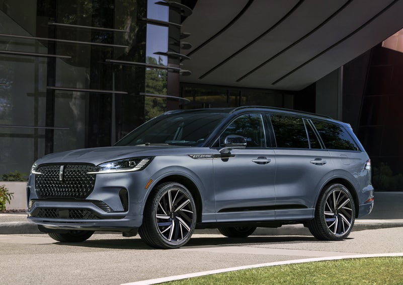 A gray 2025 Lincoln Aviator® SUV is parked outside a modern building showcasing the driver’s side of the vehicle. | Bozard Lincoln in Saint Augustine FL