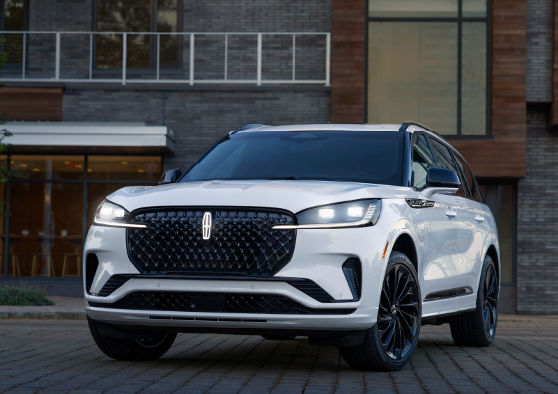 A white 2025 Lincoln Aviator® SUV is shown parked outside a modern building with gray brick and wood accents. | Bozard Lincoln in Saint Augustine FL