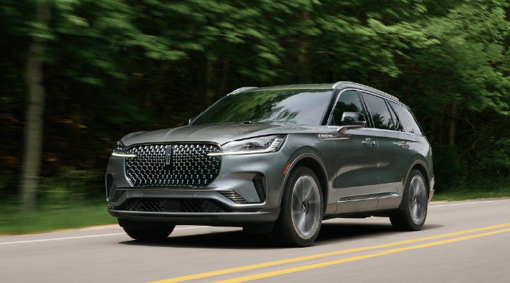 A 2027 Lincoln Aviator® SUV is being driven down a road lined with trees. | Bozard Lincoln in Saint Augustine FL